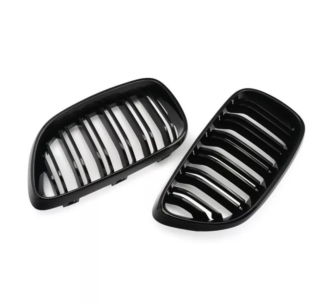 Two black, kidney-shaped car grilles with vertical slats lie on a white background, suggesting automotive parts likely used for air intake and vehicle front decoration.