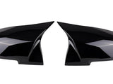 Two glossy black side mirror covers are positioned facing each other. They are streamlined, reflecting light subtly, against a plain white background.