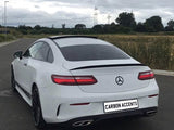 A white Mercedes coupe is parked on a road beside a grassy field under cloudy skies. The license plate reads 