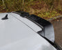 A car roof features a black roof spoiler attached to the rear. The vehicle is parked near a grassy area with trees in the background.