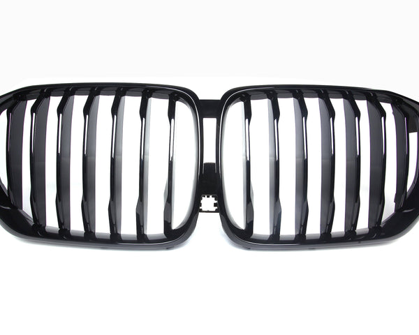 A shiny black car grille with vertical slats, forming two adjacent kidney-shaped sections, set against a plain white background.