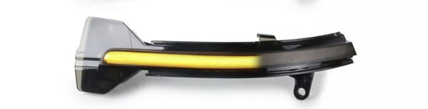 A sleek, elongated car side mirror indicator with a glowing yellow strip is mounted on a black housing, set against a plain white background.