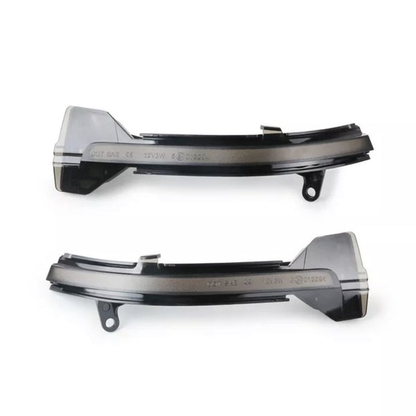 Two black, curved car parts with mounting holes, possibly side mirror indicators, rest horizontally on a plain background. Text embossed on them reads "DOT SAE CE 12V3W 01624."