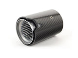A cylindrical carbon fiber exhaust tip with a perforated metal interior rests at an angle on a plain white surface, showcasing sleek design and texture contrast.