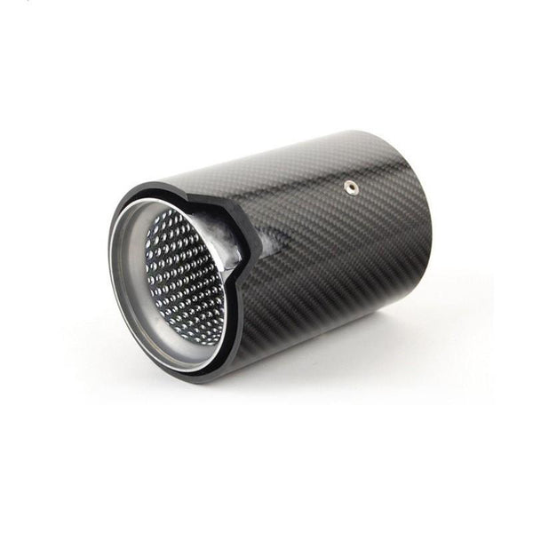 A cylindrical carbon fiber exhaust tip with a perforated metal interior rests at an angle on a plain white surface, showcasing sleek design and texture contrast.