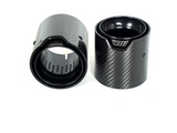 Two carbon fiber cylindrical exhaust tips are positioned upright and slightly angled against a white background. Each has a visible perforated inner surface; one displays the text 