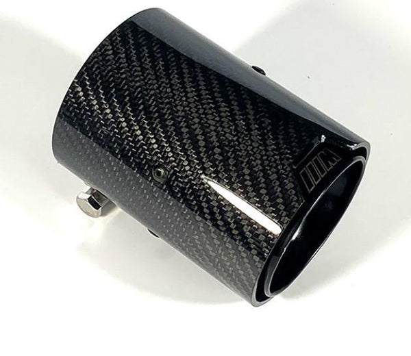 A carbon fiber exhaust tip with a glossy finish is placed on a white surface, showing a small bolt attachment and a subtle logo near the edge.