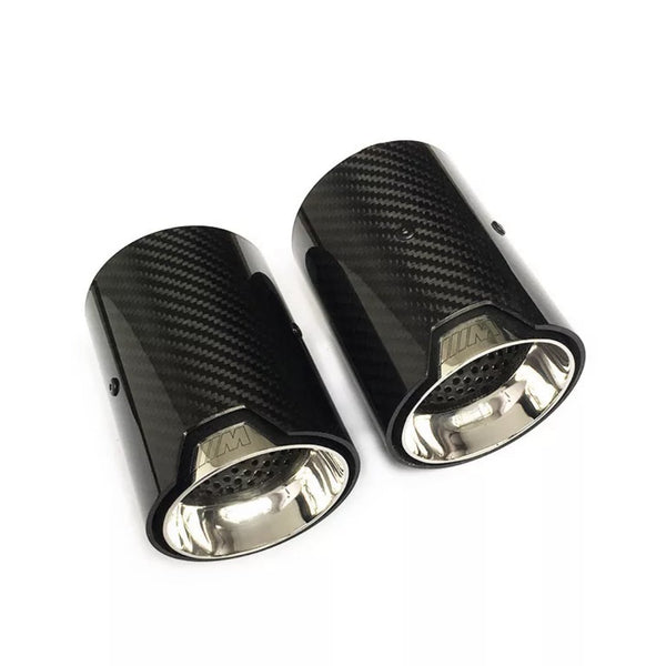 Two carbon fiber exhaust tips are displayed side by side, with a glossy black exterior and a metallic interior, on a plain white background. The text "///M" is engraved near the rims.