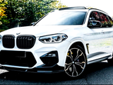 A white BMW SUV is parked on a paved road, displaying a sleek design with distinct alloy wheels and a glossy exterior, surrounded by trees in a sunlit environment.