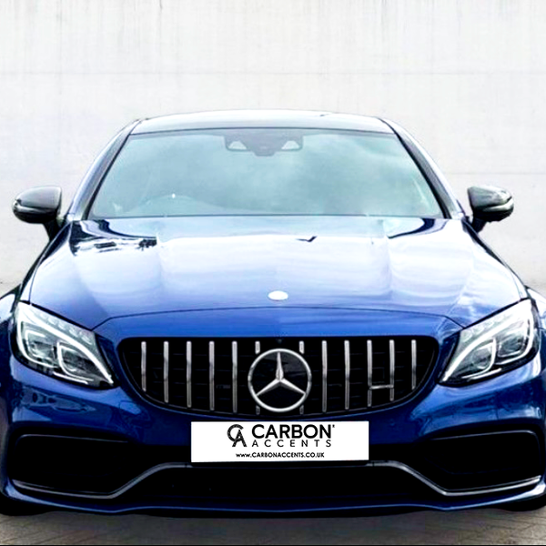 A blue luxury car is parked on a paved surface, facing forward. Its front grille features a prominent emblem. The background is a plain, light-colored wall. Text reads: "CARBON ACCENTS, WWW.CARBONACCENTS.CO.UK."