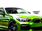 A vibrant green sports car is parked on a paved surface, featuring shiny alloy wheels and a sleek, aerodynamic design, with a blurred, bright backdrop and a visible BMW logo.
