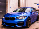 A blue BMW car is parked on a cracked surface beside an industrial building. Text on the wall includes 