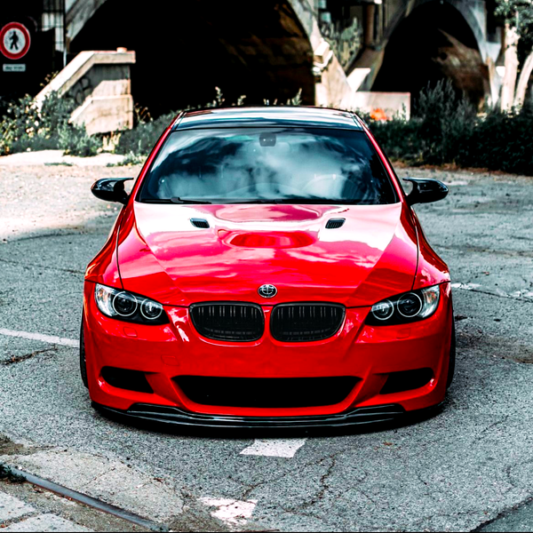 A red sports car is parked on a cracked pavement with a bridge and greenery in the background. A "no entry" sign is visible on the left side.