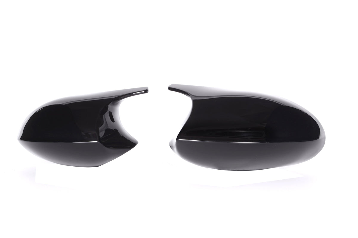 Two glossy black car side mirrors, positioned facing each other, rest against a plain white background.