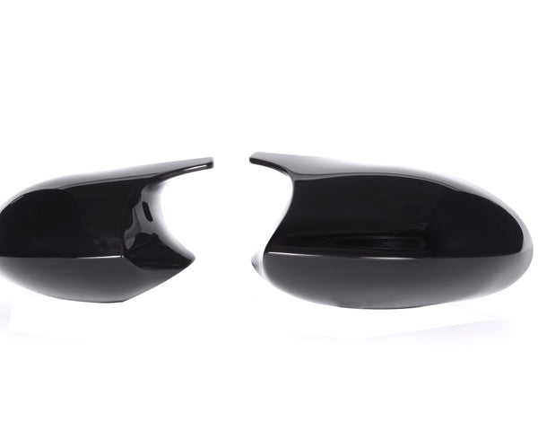 Two glossy black side mirror covers are placed against a white background, one on the left and one on the right, separated by space.