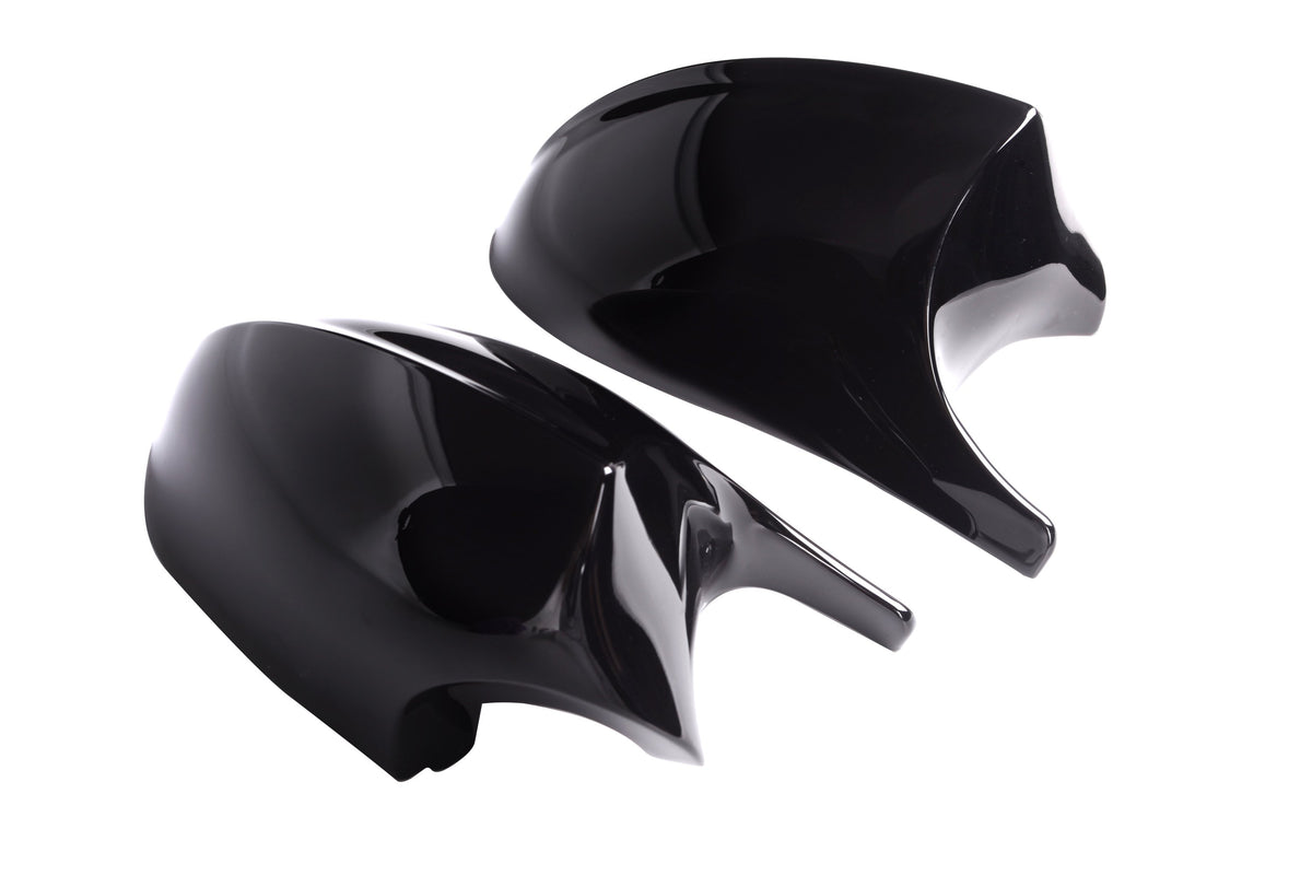 Two shiny black car mirror covers rest side by side against a plain white background, reflecting light on their smooth surfaces.