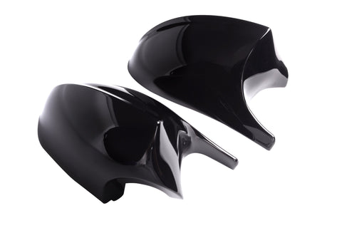 Two shiny black car mirror covers rest side by side against a plain white background, reflecting light on their smooth surfaces.