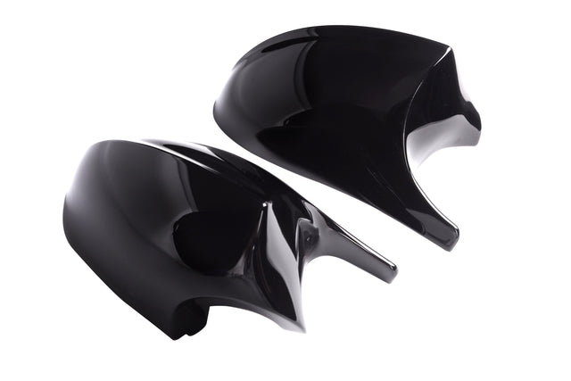Two shiny black car mirror covers rest side by side against a plain white background, reflecting light on their smooth surfaces.