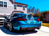 Blue BMW parked on a driveway, facing away from a two-story house. A white Kia is parked nearby, with trees and a blue sky in the background.