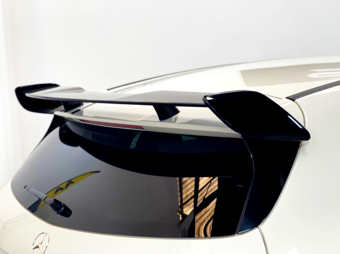 A sleek black car spoiler is mounted on the rear of a white vehicle, above a tinted back window with a visible wiper, in a well-lit indoor setting.