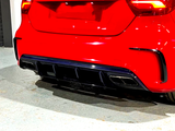 A red car's rear bumper features dual chrome exhausts and a black diffuser, parked on a light-colored concrete floor indoors.