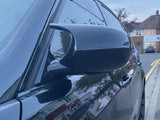 Car parked on a street, with a close-up view of the side mirror reflecting adjacent houses, under a cloudy sky in a residential neighborhood.