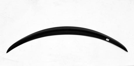 A sleek, curved black object, resembling a long crescent, lies on a plain white surface. A small white rectangular label is attached near one end.
