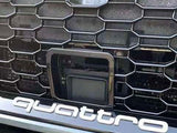A car grille features a prominent honeycomb pattern. Centered is a rectangular sensor or camera. Below, bold white lettering spells 