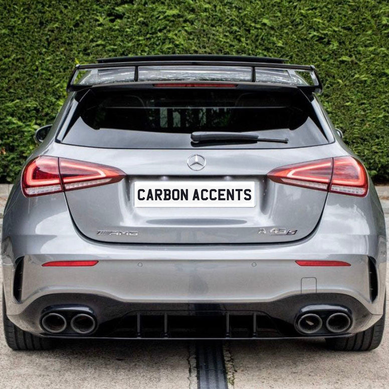 A silver Mercedes-Benz hatchback (AMG A 45 S) is parked on concrete. The license plate reads "CARBON ACCENTS," with dense greenery in the background.