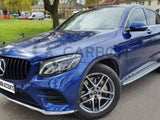 A blue Mercedes car parked on a road with a side view of large alloy wheels. Background features a grassy area with trees and buildings. Text: 