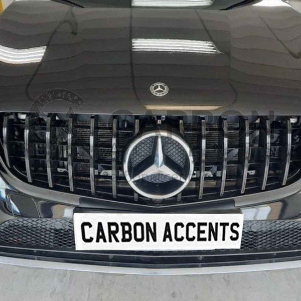 A black car front features a prominent grille with a star emblem and modern headlights, parked indoors. The license plate reads "CARBON ACCENTS."