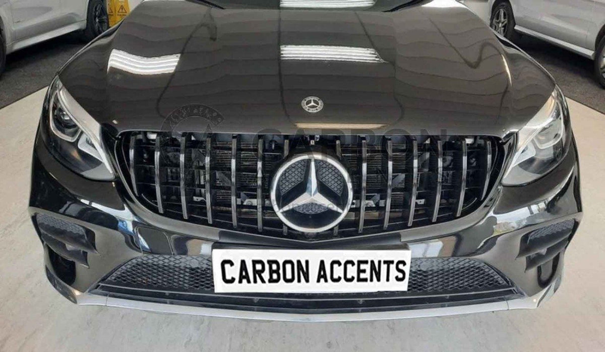 A black car front features a prominent grille with a star emblem and modern headlights, parked indoors. The license plate reads "CARBON ACCENTS."