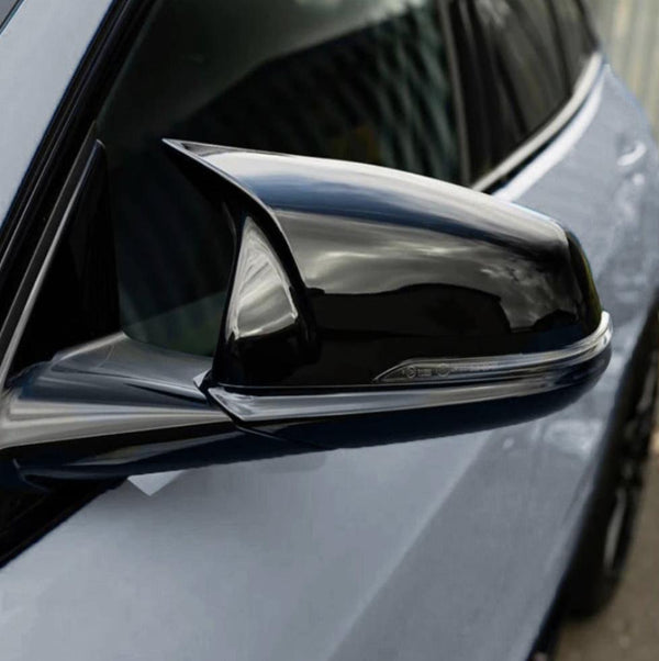 A sleek, shiny side mirror on a car reflects its surroundings in close-up view, showcasing its aerodynamic design, with a blurred urban backdrop in the distance.