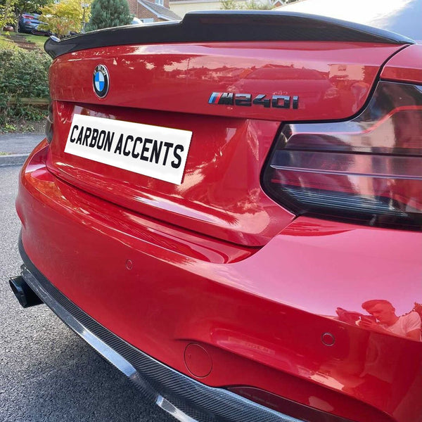 Red BMW M240i with carbon accents parked on residential street. "CARBON ACCENTS" text on license plate. Background includes houses and trees.