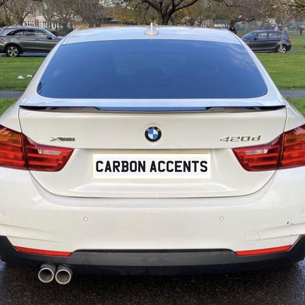 A white BMW 420d is parked on a paved path, with "CARBON ACCENTS" displayed on its license plate, surrounded by green lawns and other parked cars in a park setting.