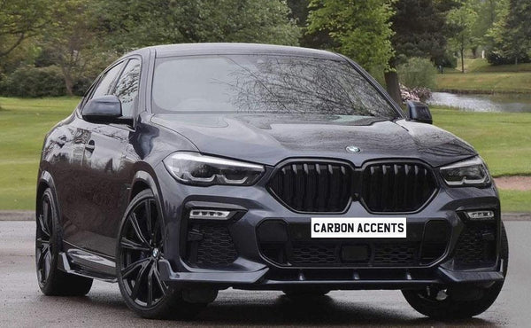 A sleek dark-colored BMW SUV is parked on a paved surface, surrounded by lush greenery and a pond. The license plate reads "CARBON ACCENTS."